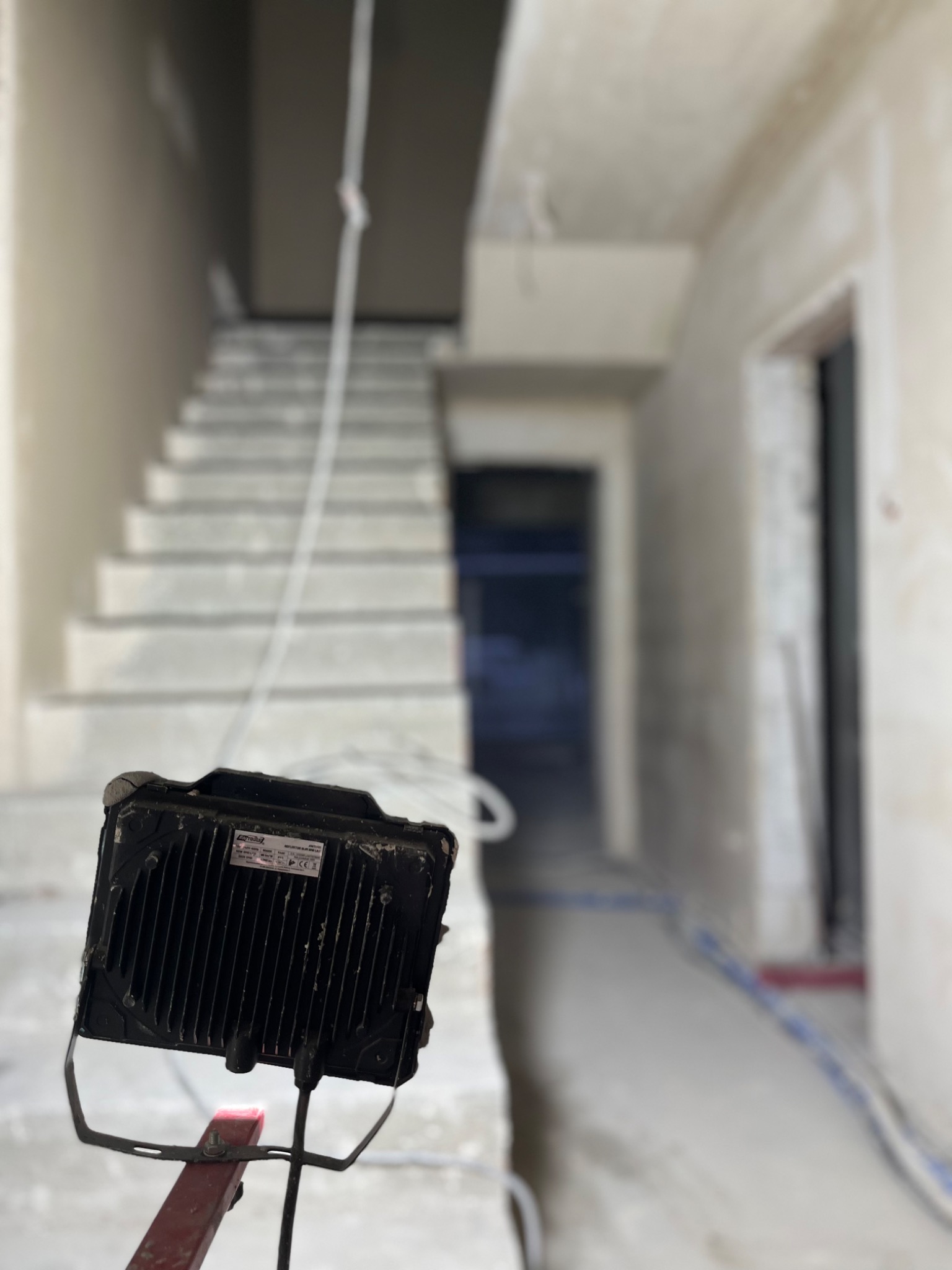 Świeżo otynkowane schody i korytarz w surowym stanie, oświetlone halogenem na statywie, widok z dołu.