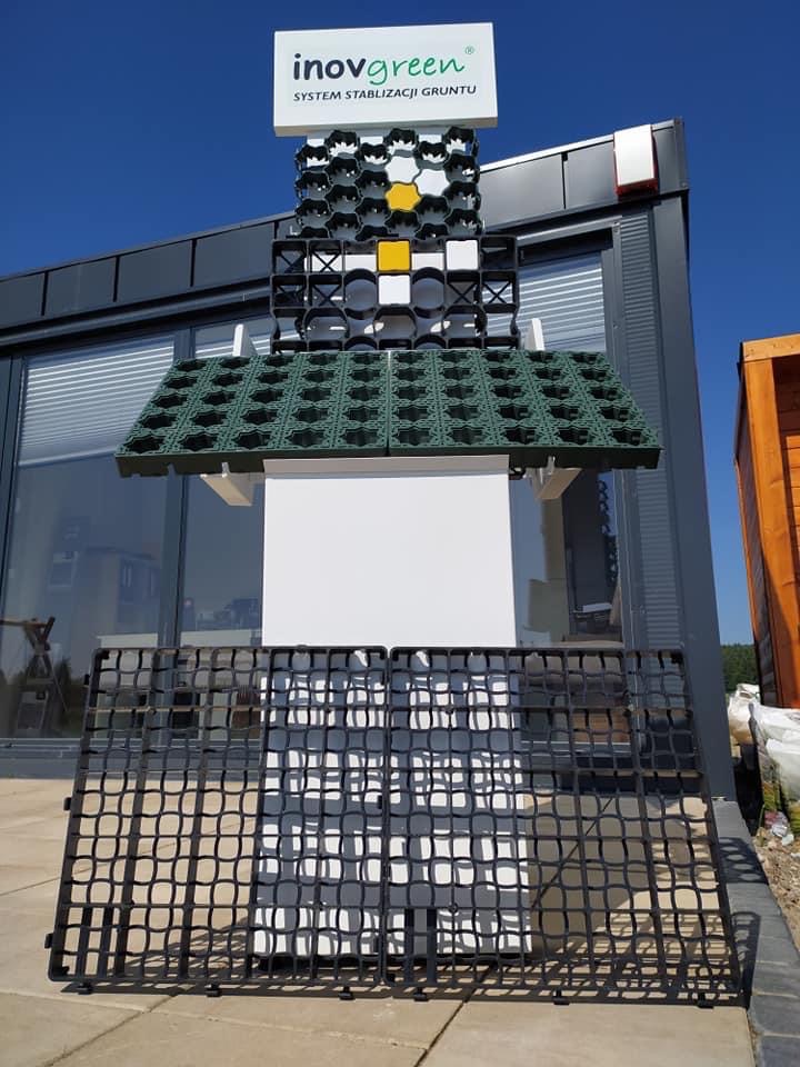 Ekspozycja systemu stabilizacji gruntu Inovgreen z modułowych paneli w kolorach czarnym, białym, żółtym i zielonym, ustawionych na zewnątrz budynku.