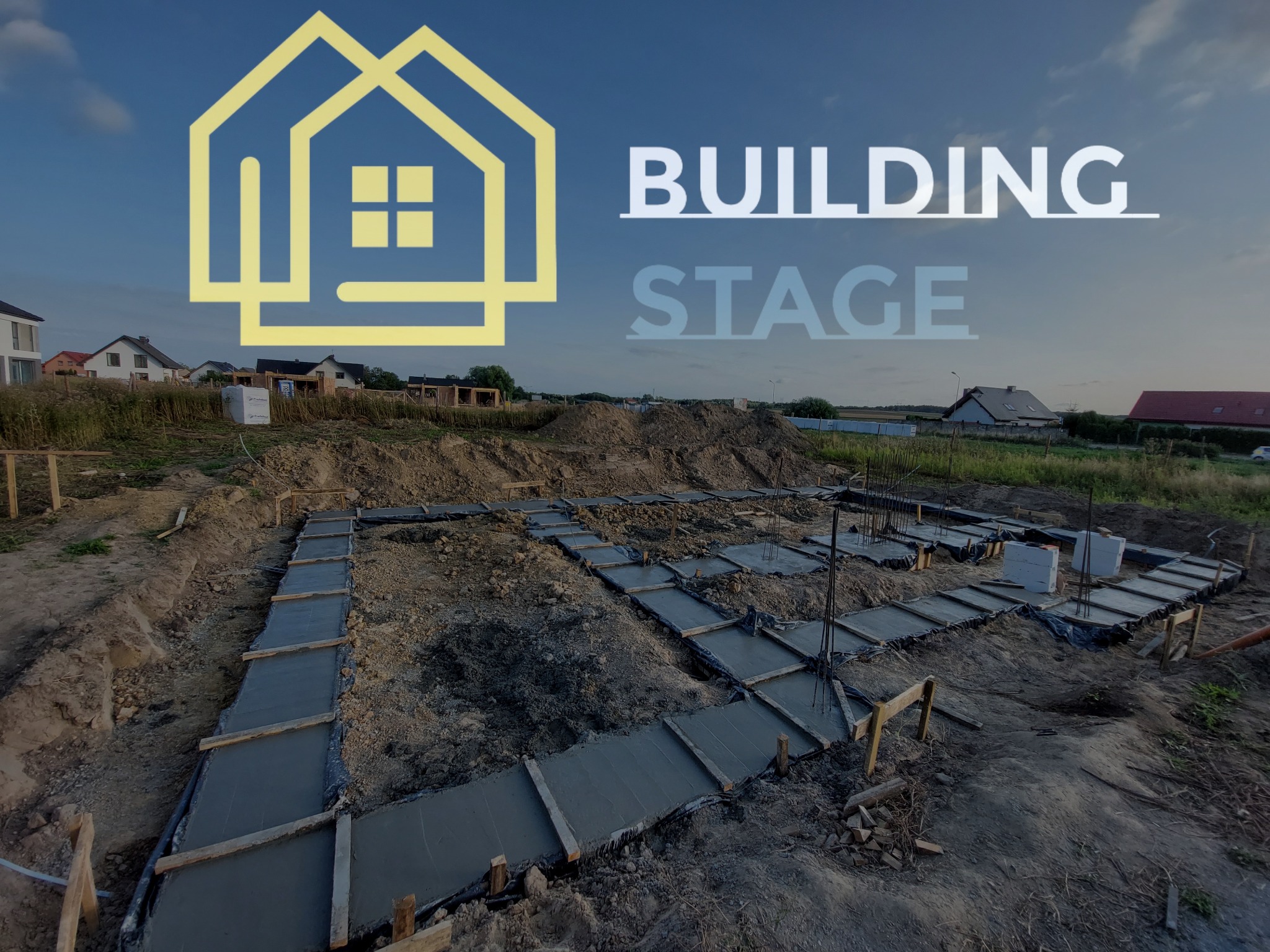 Wylane betonowe ławy fundamentowe w szalunkach drewnianych z wystającymi zbrojeniami, widok z góry na plac budowy z domami w tle.