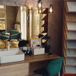 Nowoczesna aranżacja łazienki z blatem drewnianym, umywalką nablatową i lustrem odbijającym salonik w tle, obok regał z próbkami wykończeń meblowych.