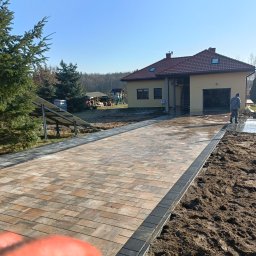 PHU Eurokop Justyna Zagaja - Umyta ciśnieniowo, ułożona z kostki brukowej ścieżka prowadząca do domu z garażem, widoczne panele słoneczne i pracownik w oddali.