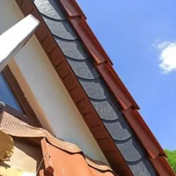 Montaż paneli elewacyjnych imitujących łupek na poddaszu w Krzęcinie, widoczne fragmenty rusztowania i nieba.