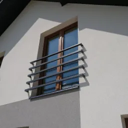 Zewnętrzne, metalowe balustrady okienne w nowoczesnym domu z jasną elewacją i ciemnym dachem.