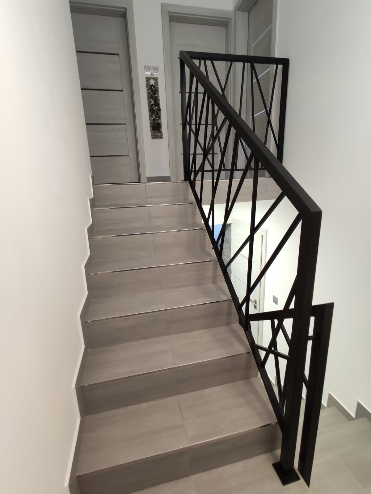 Schody wyłożone szarymi płytkami z czarną, geometryczną barierką, widok z góry