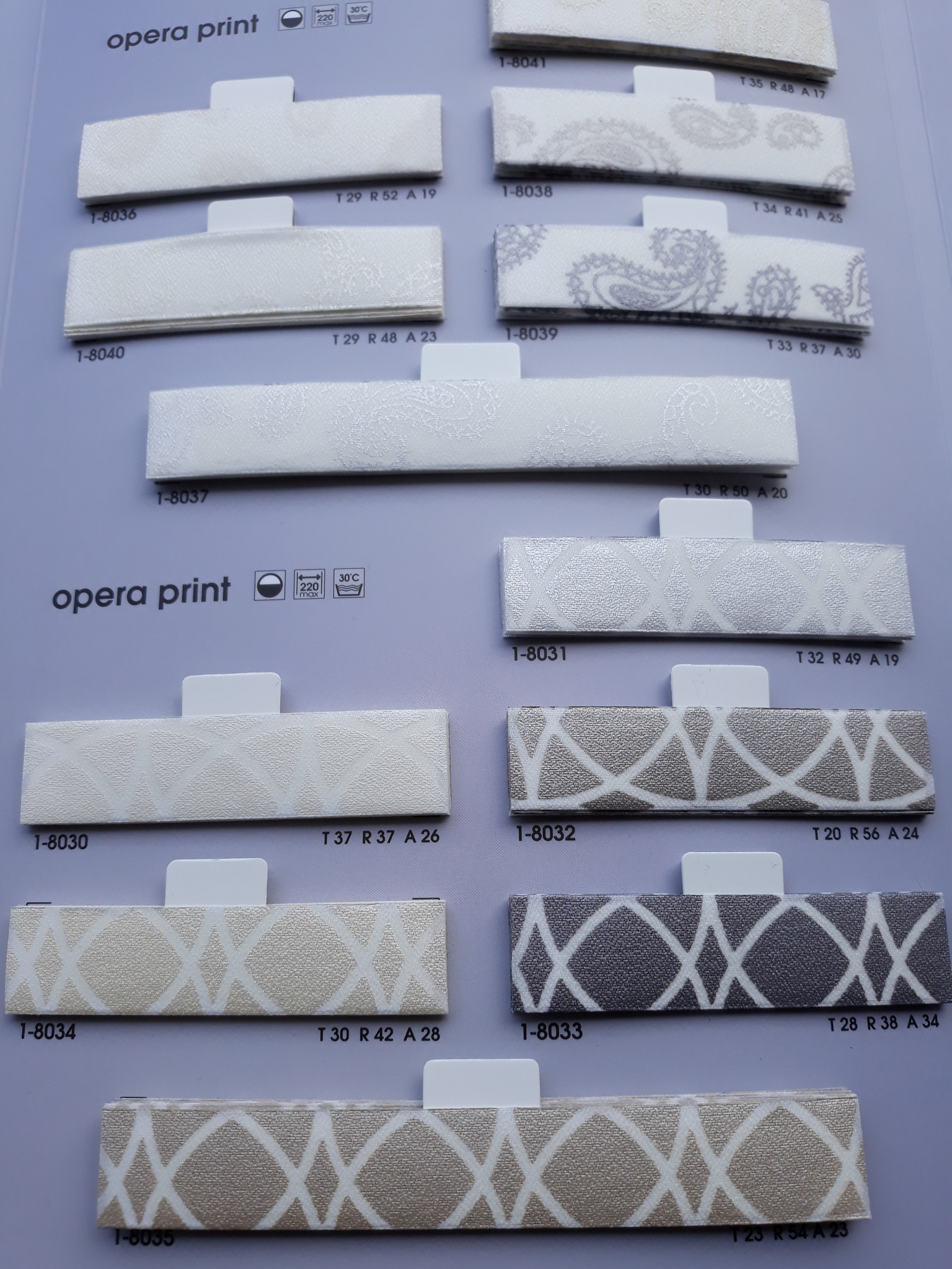 Katalog próbek tkanin do rolet i żaluzji z różnymi wzorami, ułożonych na szarym tle, z widocznymi numerami identyfikacyjnymi i informacjami o składzie.