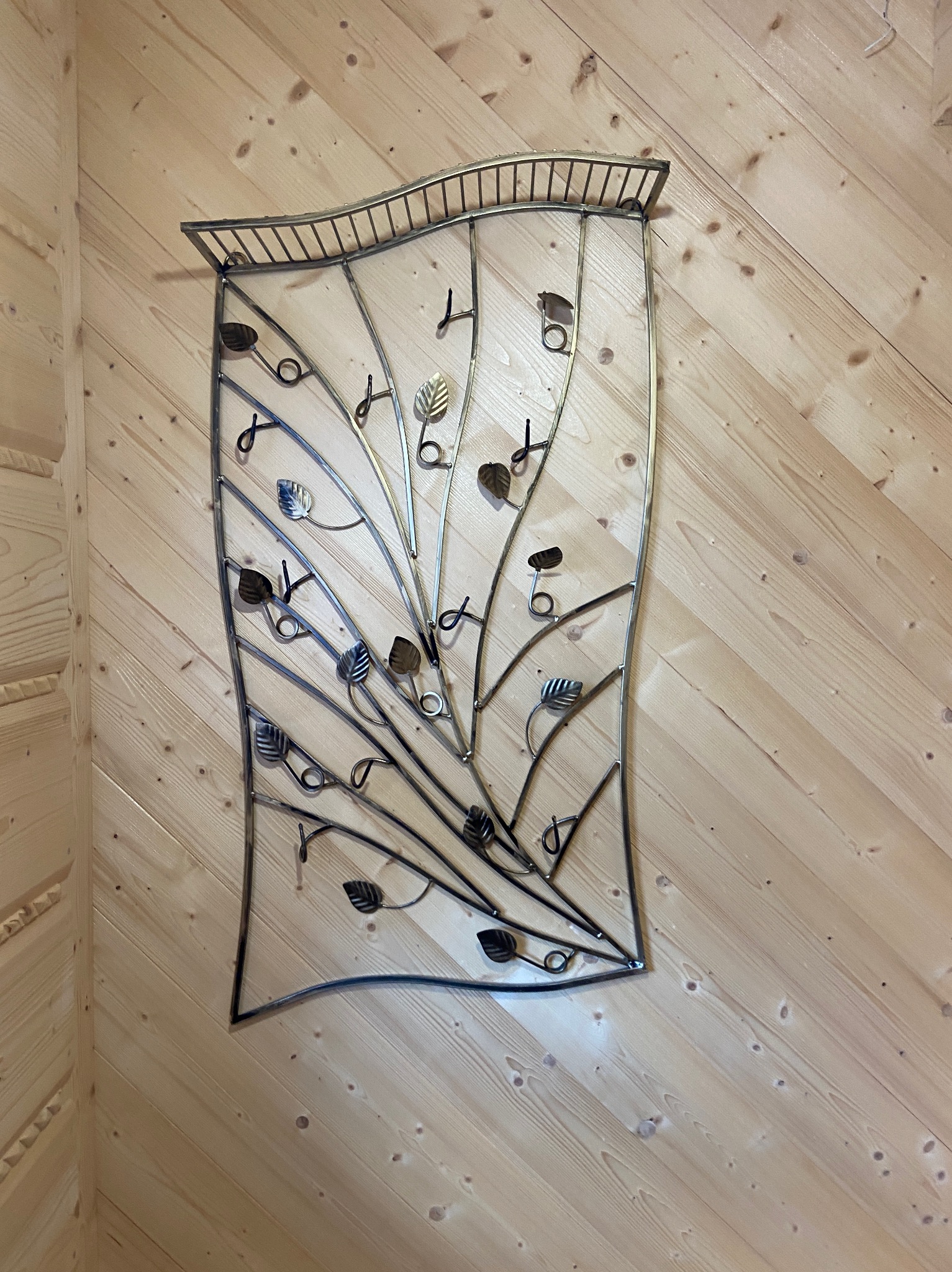 Metalowy wieszak na klucze w kształcie drzewa z liśćmi, zamontowany na drewnianej ścianie z boazerii. Dekoracyjny element wykończenia wnętrza.