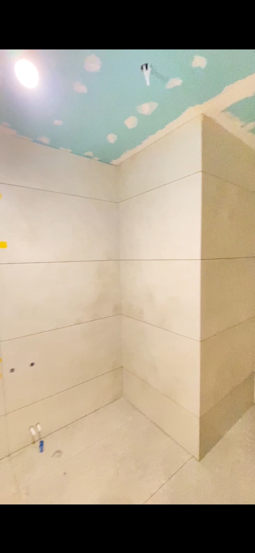 Wnętrze w trakcie wykańczania: ściany z płyt kartonowo-gipsowych z widocznymi łączeniami, sufit z niebieską farbą i punktowymi łatami gipsu. Widoczne instalacje.