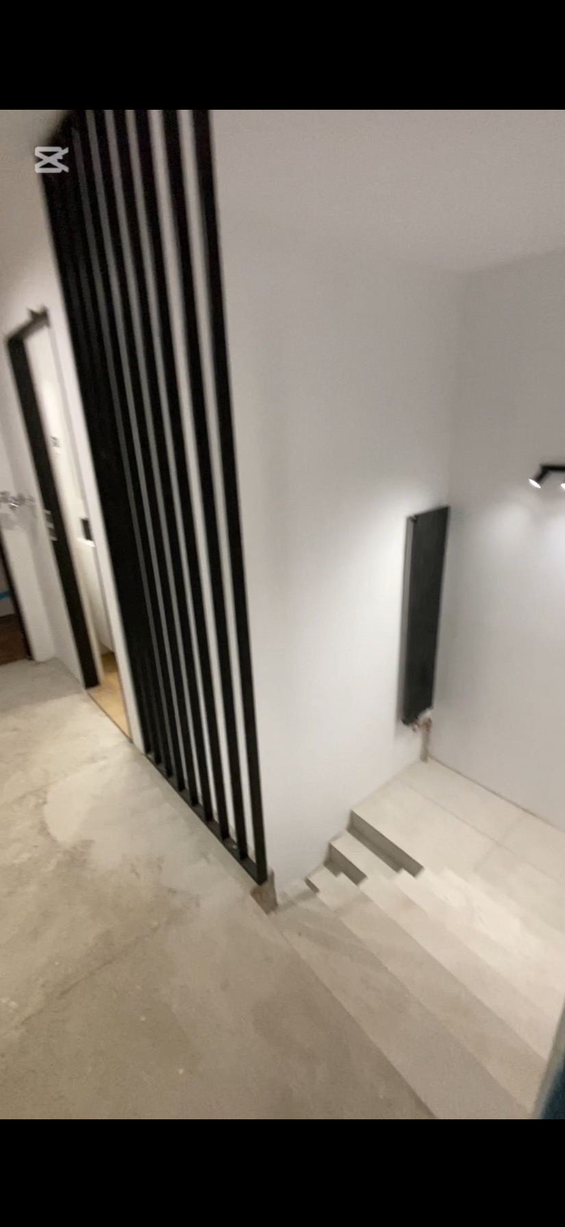 Nowoczesne schody z jasnymi płytkami i czarną balustradą z pionowych listew. Minimalistyczny design wnętrza z grzejnikiem na ścianie.