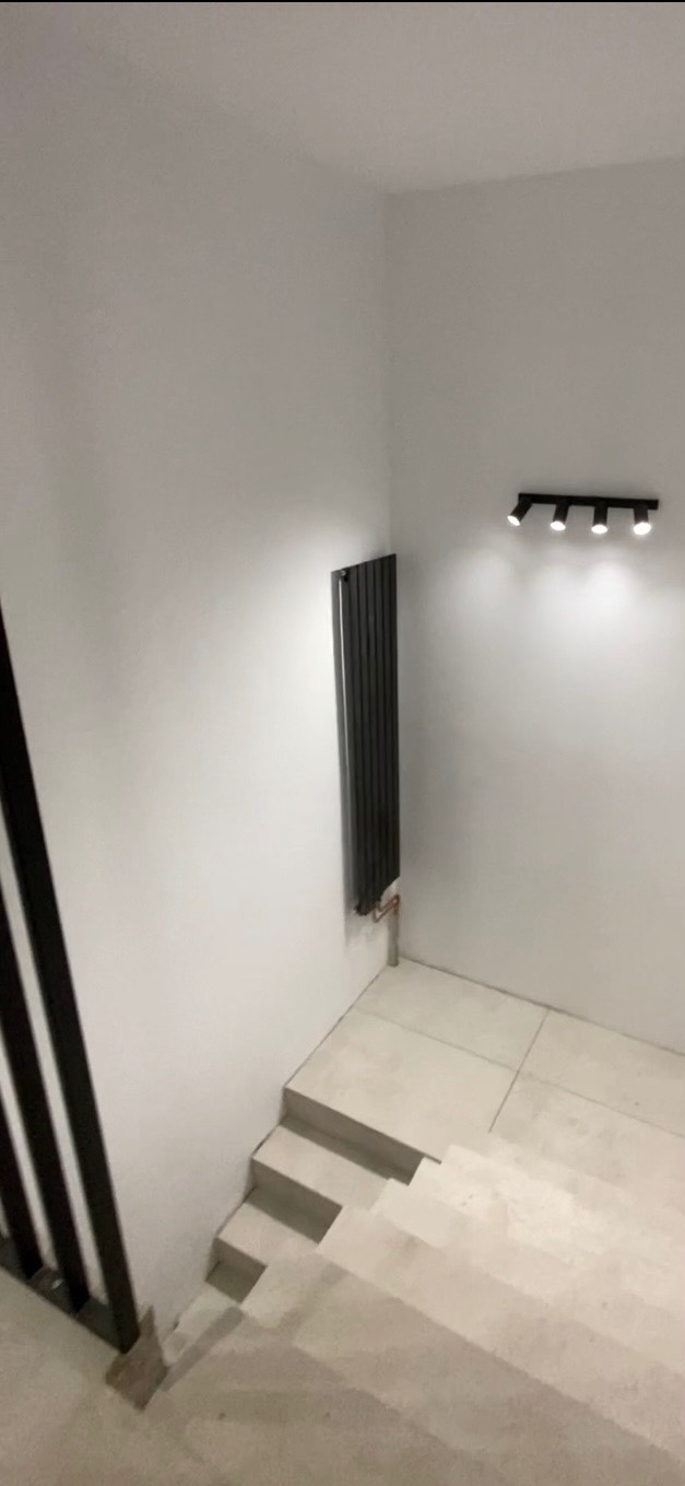 Minimalistyczne wnętrze: szare schody, grzejnik panelowy i oświetlenie punktowe na białej ścianie. Ujęcie z góry, podkreślające nowoczesny design.
