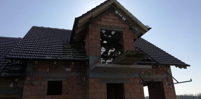 Niedokończony budynek z cegły z częściowo pokrytym dachem z ciemnej dachówki i odsłoniętą konstrukcją więźby dachowej w lukarnie.