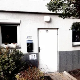 Wejście do biura rachunkowego RENDOR przy ulicy Łamanej 14 we Włochach, Warszawa. Na ścianie tabliczka z nazwą ulicy i numerem budynku, skrzynka pocztowa z numerem 25, okno z kwiatami i informacja...