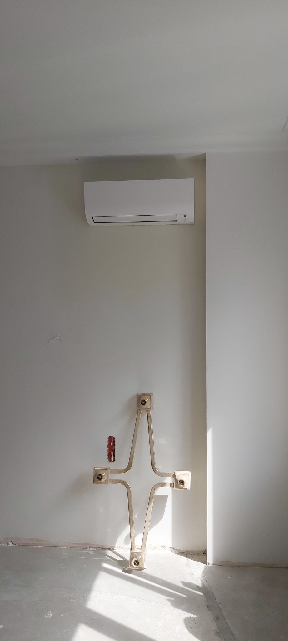 Biały klimatyzator ścienny zamontowany nad instalacją hydrauliczną w surowym wnętrzu podczas remontu.