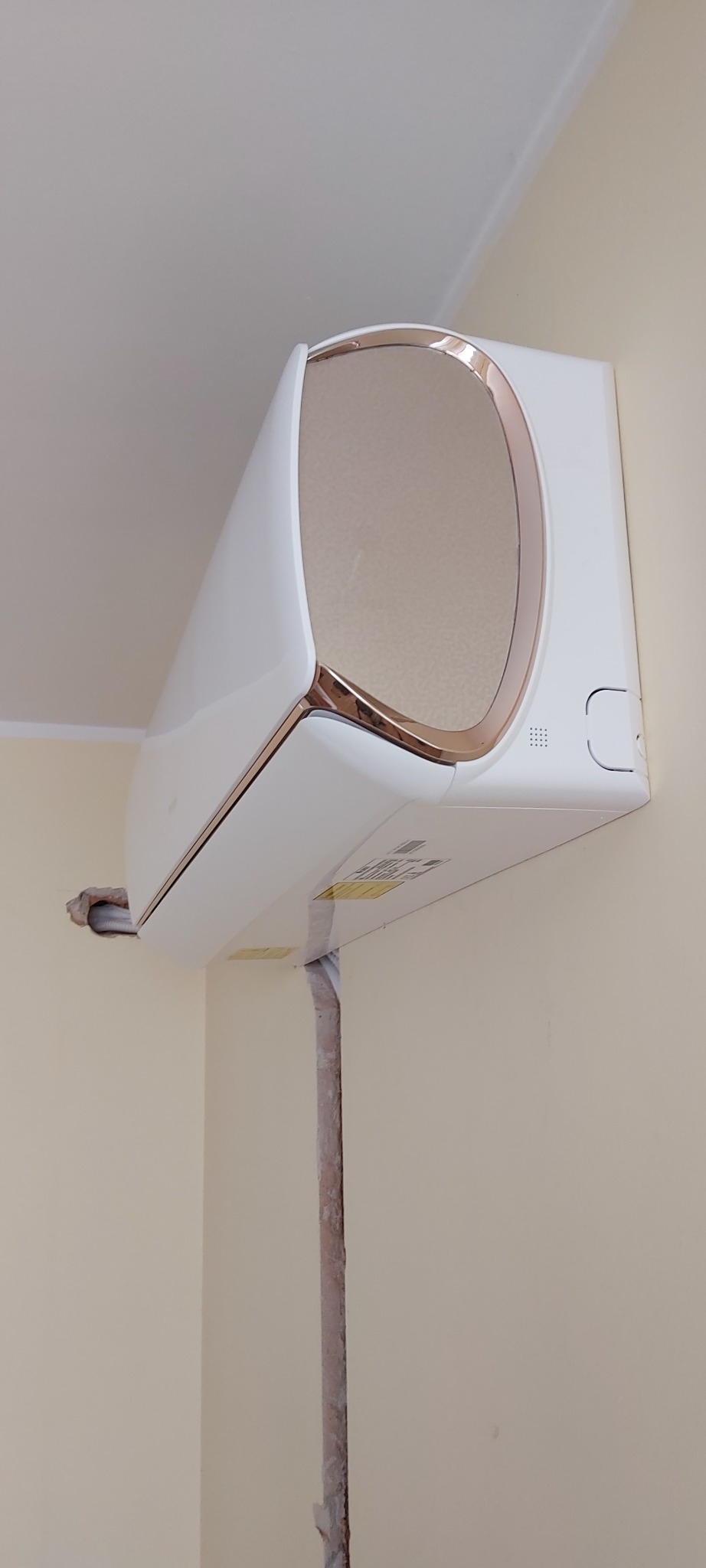 Biały klimatyzator z miedzianymi akcentami zamontowany na beżowej ścianie w mieszkaniu w Warszawie, widoczna instalacja odprowadzająca skropliny.