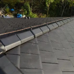 Czarny dach z dachówki ceramicznej z zamontowanym systemem odgromowym w postaci miedzianego przewodu i uchwytów, widok z góry