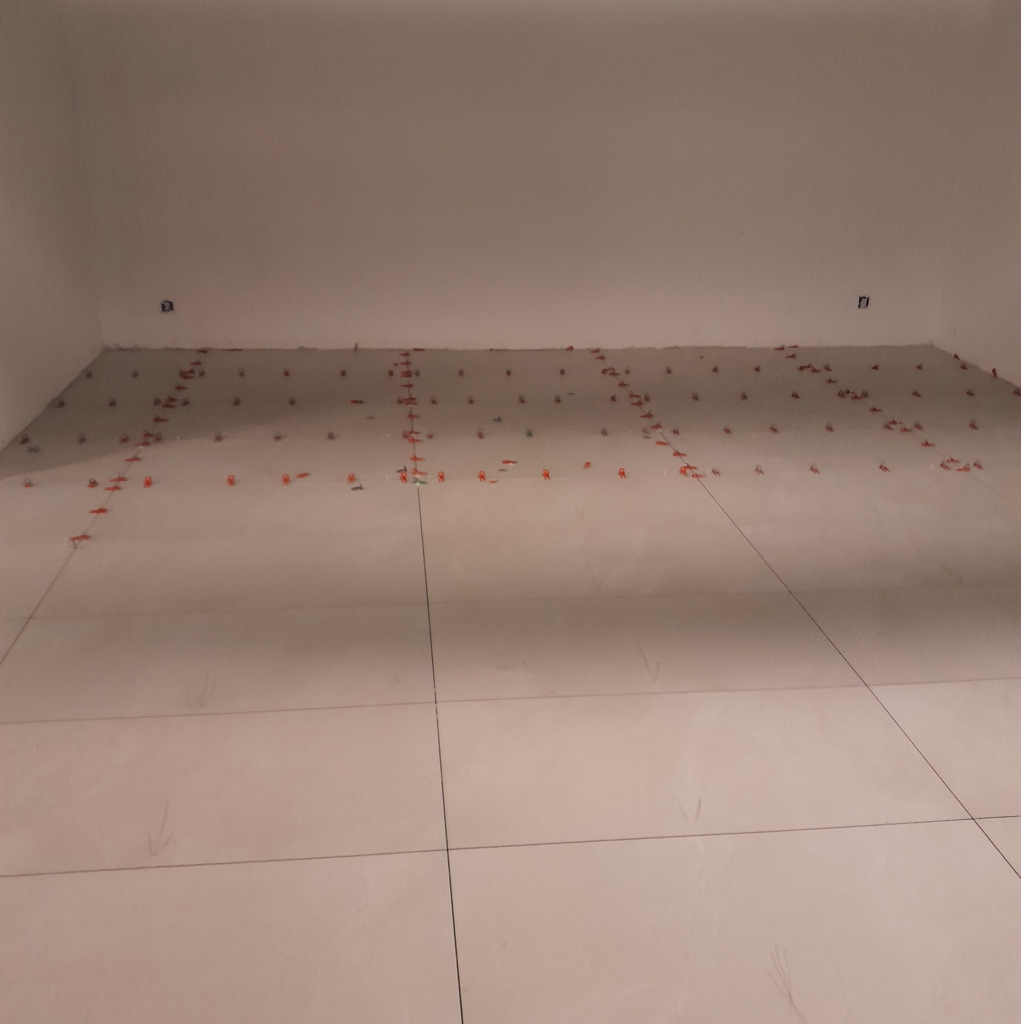 Ułożone, jasne płytki podłogowe z czerwonymi krzyżykami dystansowymi w pomieszczeniu. Usługa glazurnicza w Niwiskach.