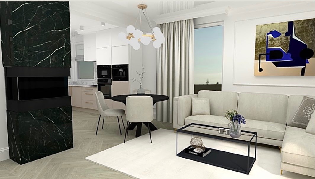 Wnętrze salonu połączonego z kuchnią, z czarnym marmurowym kominkiem, okrągłym czarnym stołem i beżową sofą narożną, oświetlone nowoczesną lampą wiszącą.