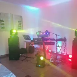 Scena oświetlona kolorowymi światłami, z klawiaturą, mikrofonem i nagłośnieniem, przygotowana do występu na imprezie, widoczny baner reklamowy z nazwą zespołu.