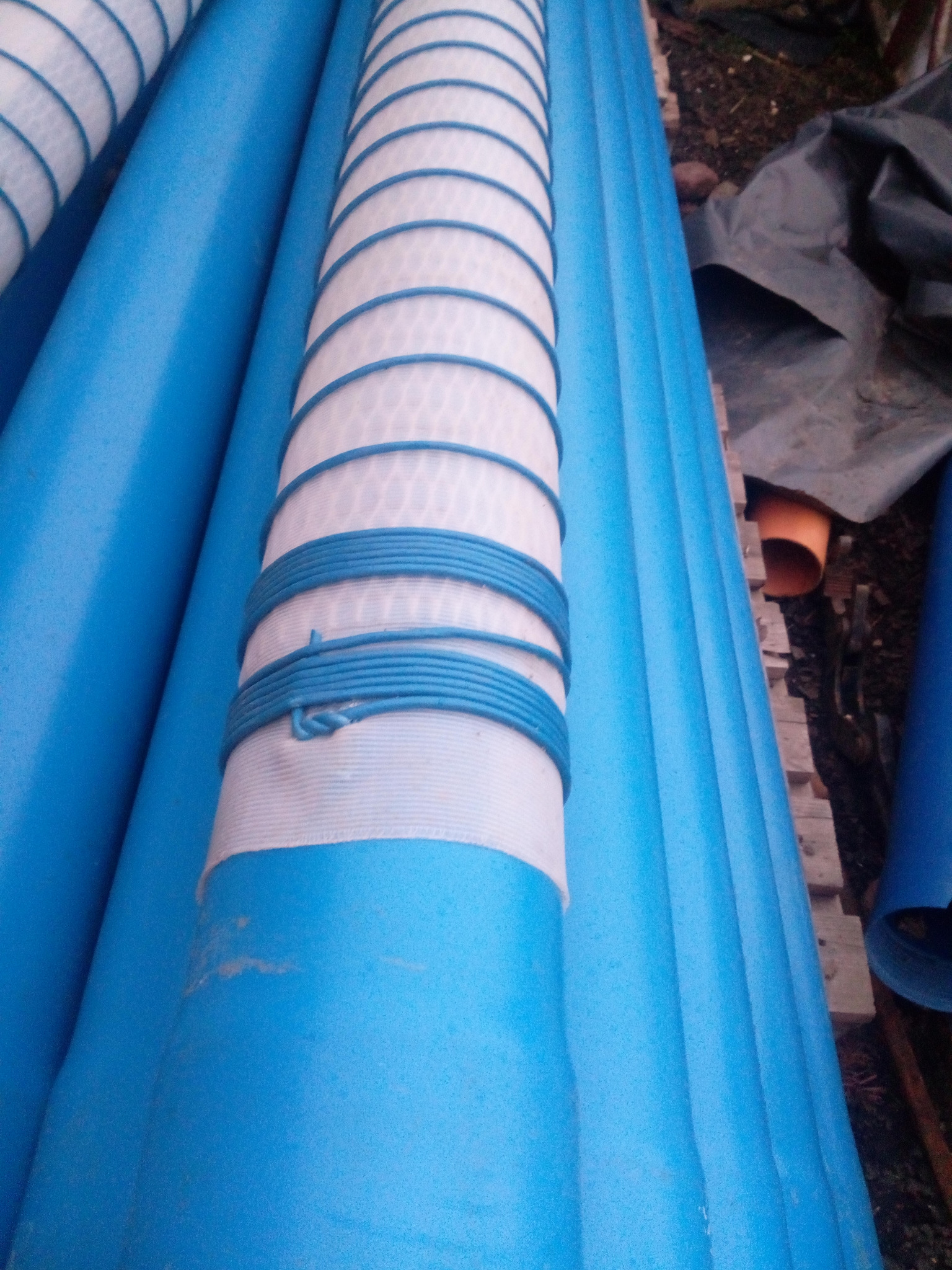 Niebieskie rury do wiercenia studni głębinowych z owijką filtrującą, zabezpieczone niebieskim sznurkiem, ułożone obok siebie.