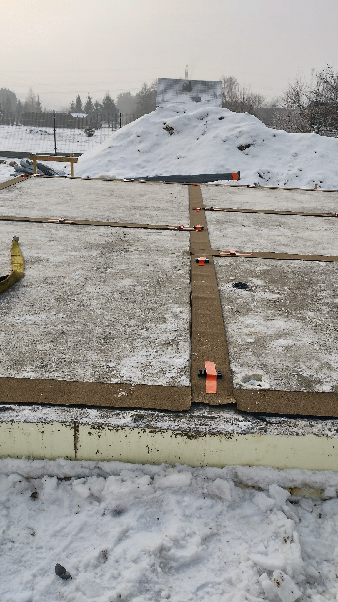 Płyta fundamentowa z izolacją poziomą i podkładkami rektyfikacyjnymi w zimowej scenerii. Widoczne elementy konstrukcyjne i śnieg.