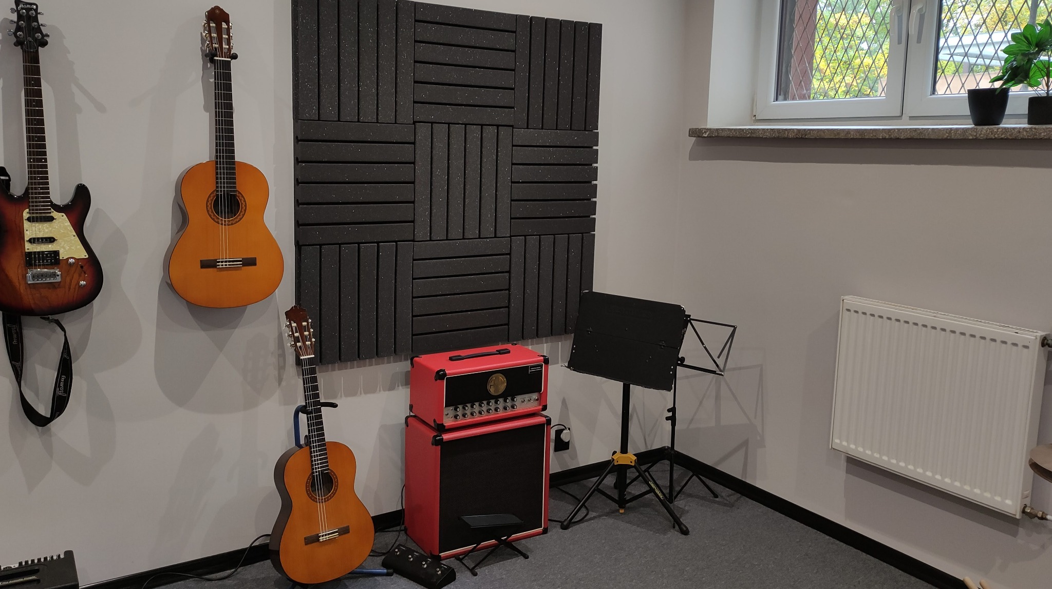 Pokój do nauki gry na gitarze z panelami akustycznymi, wzmacniaczem, pulpitem na nuty i trzema gitarami wiszącymi na ścianie.