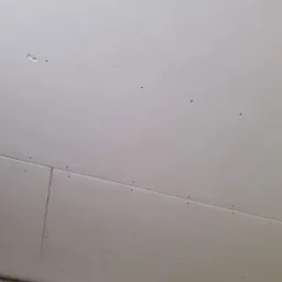 Połączenie płyt karton-gips na suficie, widoczne wkręty mocujące, przygotowane do szpachlowania. Jedna z płyt ma niewielkie uszkodzenie.