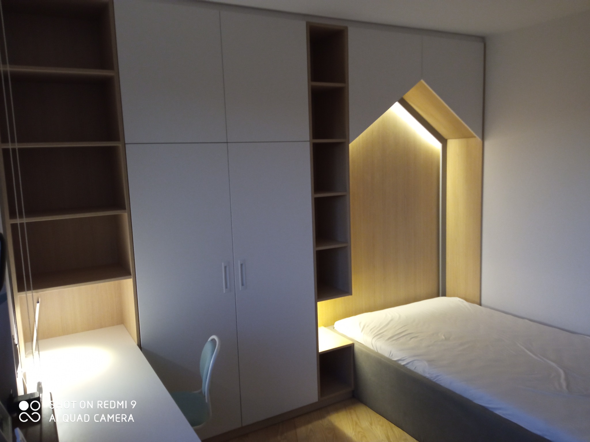 Biała zabudowa meblowa w pokoju młodzieżowym z biurkiem, szafą i łóżkiem z podświetlaną wnęką w kształcie domku.