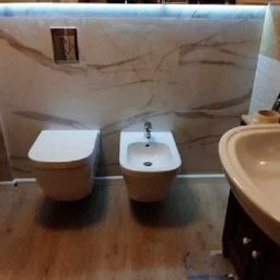 Pracownia - Wykończona łazienka w Bydgoszczy z toaletą, bidetem i umywalką na tle marmurowych płytek z subtelnym oświetleniem LED