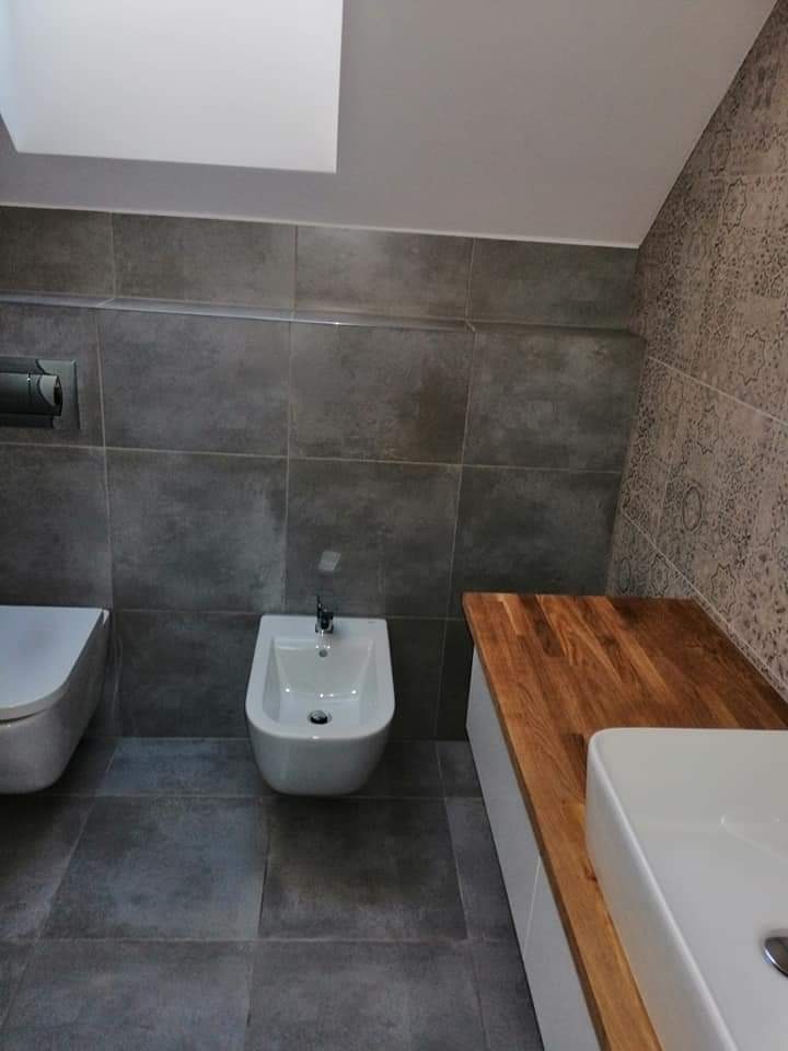 Nowoczesna łazienka w szarościach z drewnianym blatem, widoczne WC, bidet i umywalka nablatowa, na ścianie płytki w dwa różne wzory.