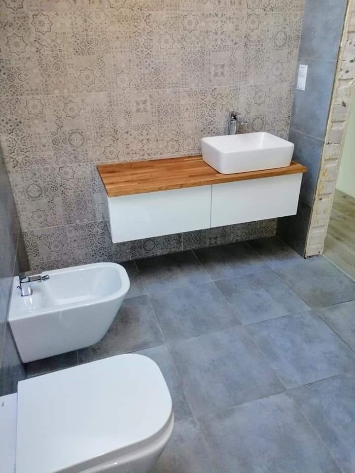 Nowoczesna łazienka z szarą płytką podłogową i ścienną w marokańskie wzory, biała umywalka nablatowa na drewnianym blacie, bidet i toaleta.