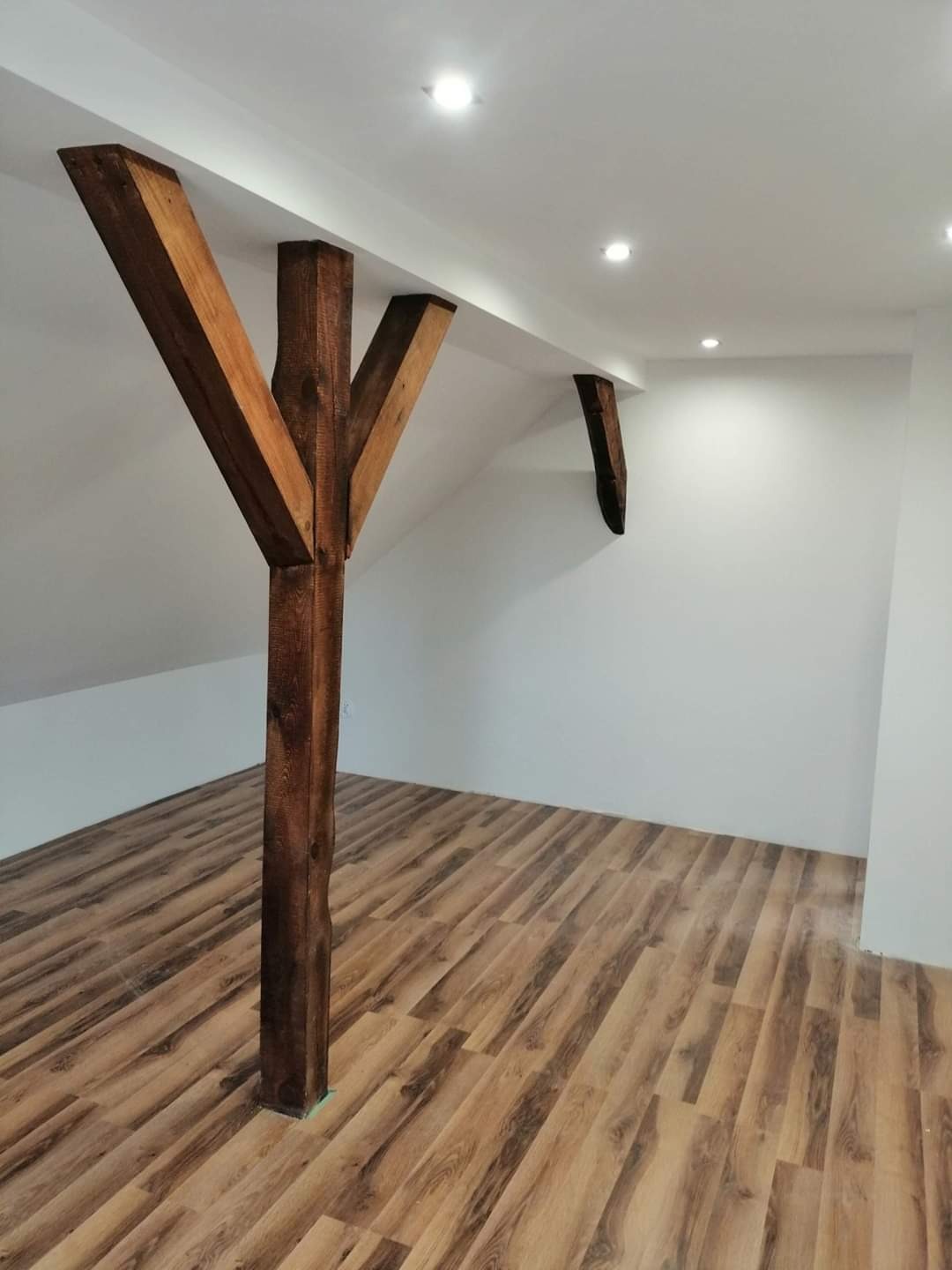 Drewniany słup podtrzymujący strop w wykończonym pokoju na poddaszu z panelami podłogowymi imitującymi drewno.