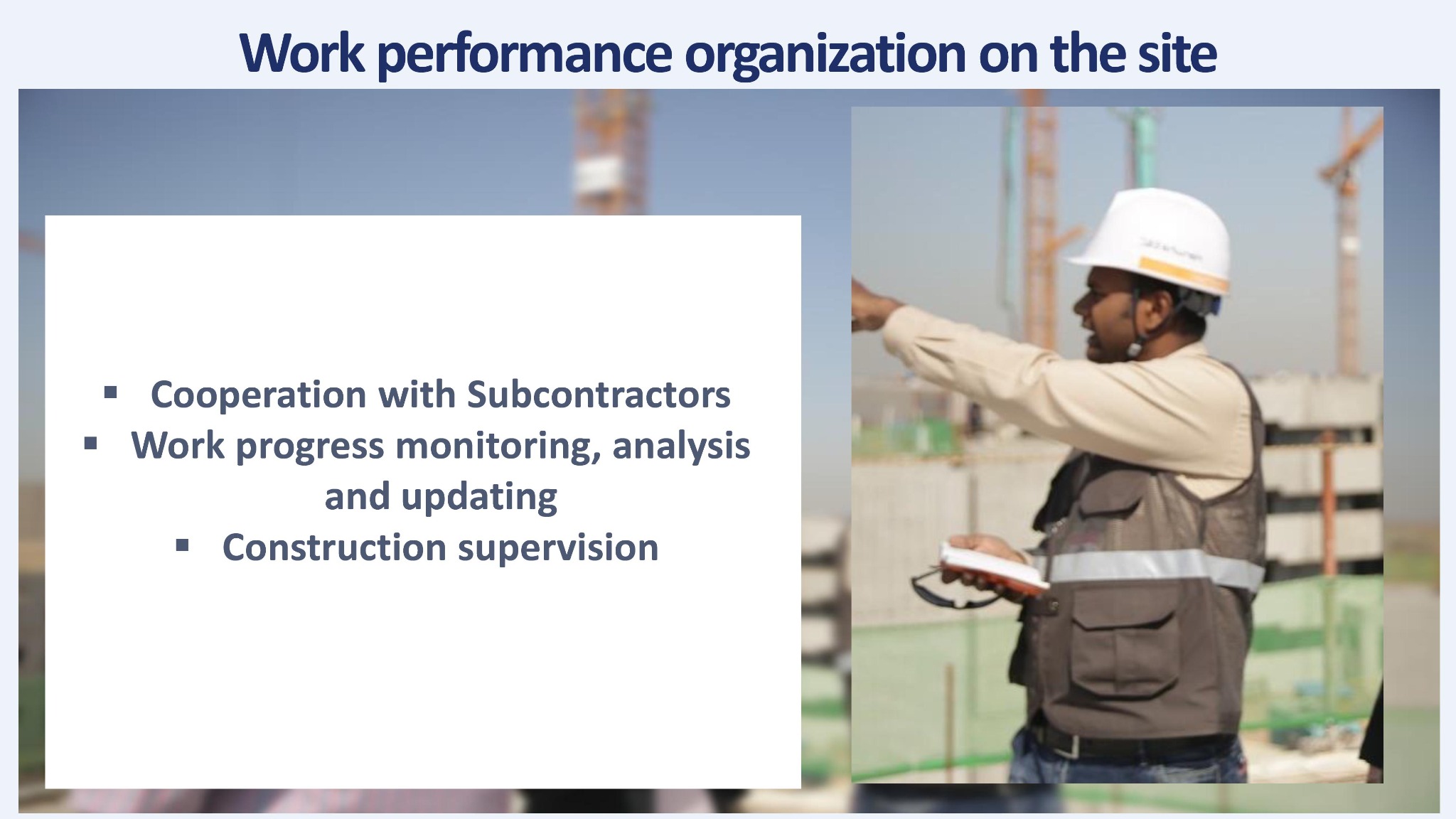 Inżynier w kasku i kamizelce odblaskowej nadzoruje budowę, wskazując na konstrukcję w tle i trzymając notatnik.