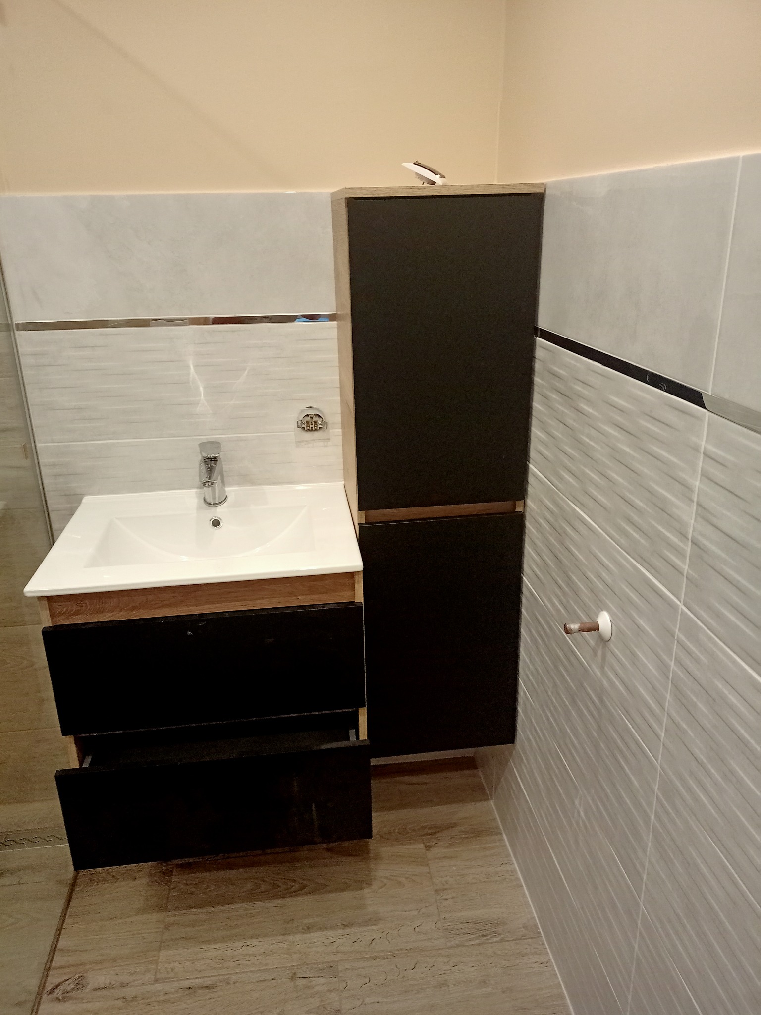 Nowoczesna łazienka po renowacji: umywalka nablatowa z szafką z czarnymi frontami, wisząca szafka w tym samym kolorze, płytki imitujące marmur na ścianach i podłodze.