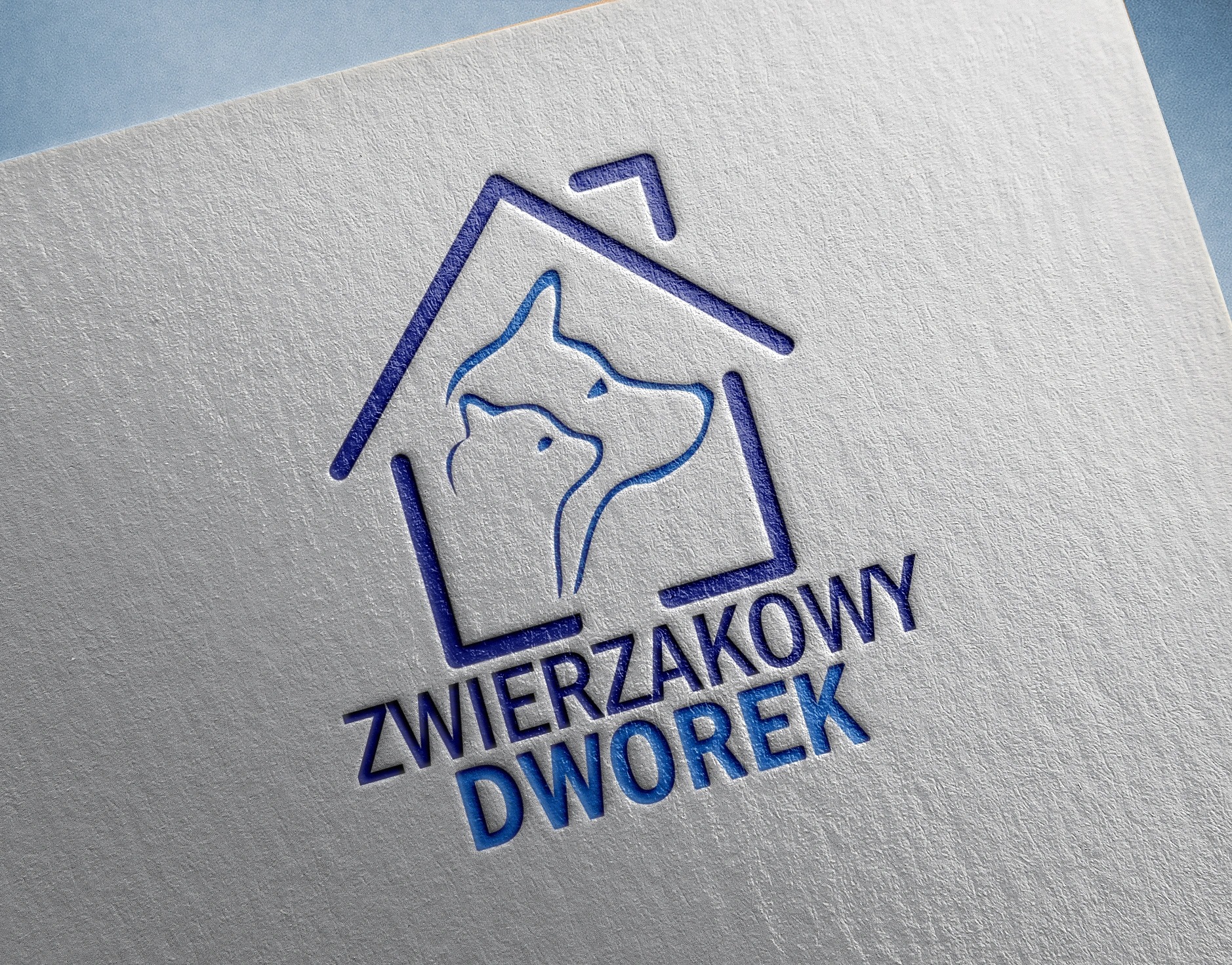 Niebieski, wytłoczony logotyp 'Zwierzakowy Dworek' przedstawiający zarys domu z sylwetkami psa i kota na fakturowanym, białym papierze.