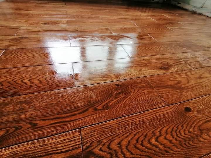 Błyszcząca, świeżo położona podłoga z paneli imitujących drewno, widoczne odbicie światła od okna, ciepła kolorystyka brązu i beżu.