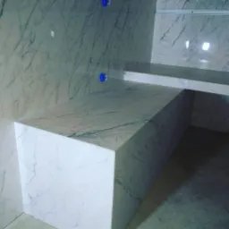 Wykończona łazienka z blatem i ścianami z białego marmuru z delikatnym szarym żyłkowaniem, widoczne niebieskie elementy montażowe.