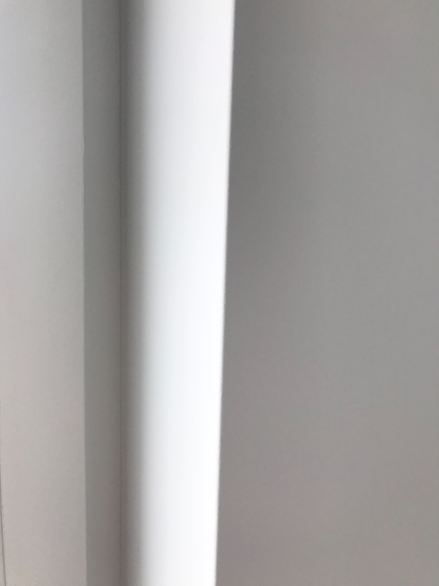 Świeżo pomalowany narożnik pokoju w odcieniach bieli, z widocznym załamaniem światła na pionowej krawędzi ściany.