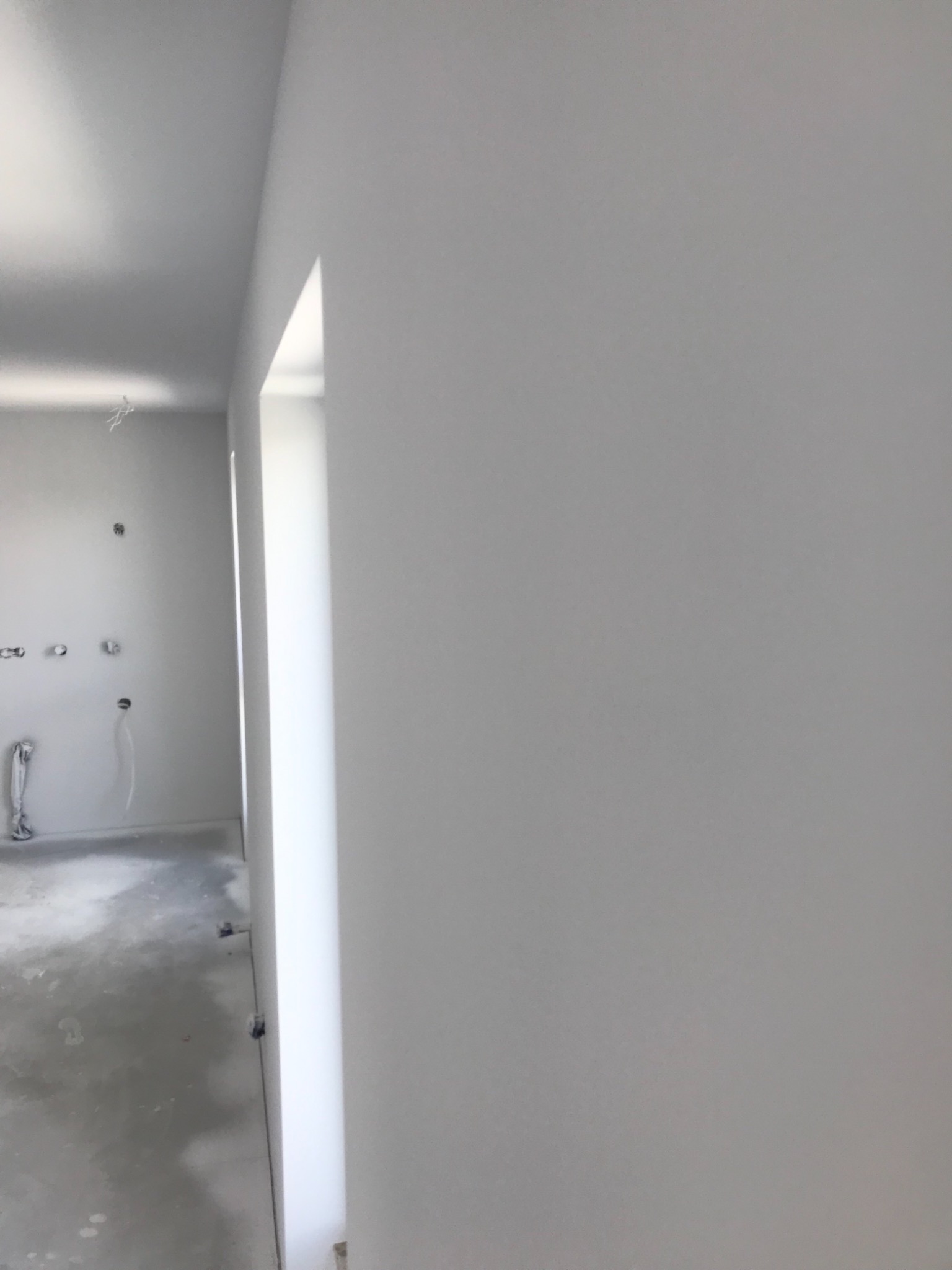 Świeżo wykończone, jasnoszare ściany w nowym mieszkaniu, widoczne kable i instalacje elektryczne przed montażem osprzętu, surowy beton na podłodze.