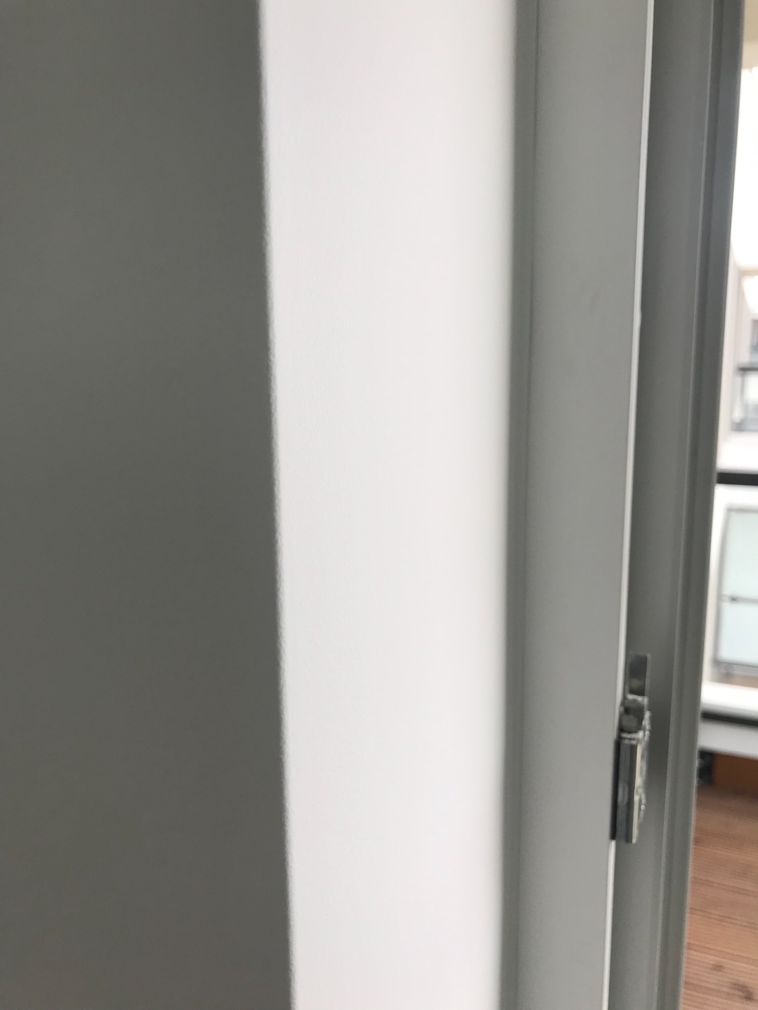 Fragment świeżo pomalowanej, białej ściany przy futrynie drzwi z widocznym zamkiem.