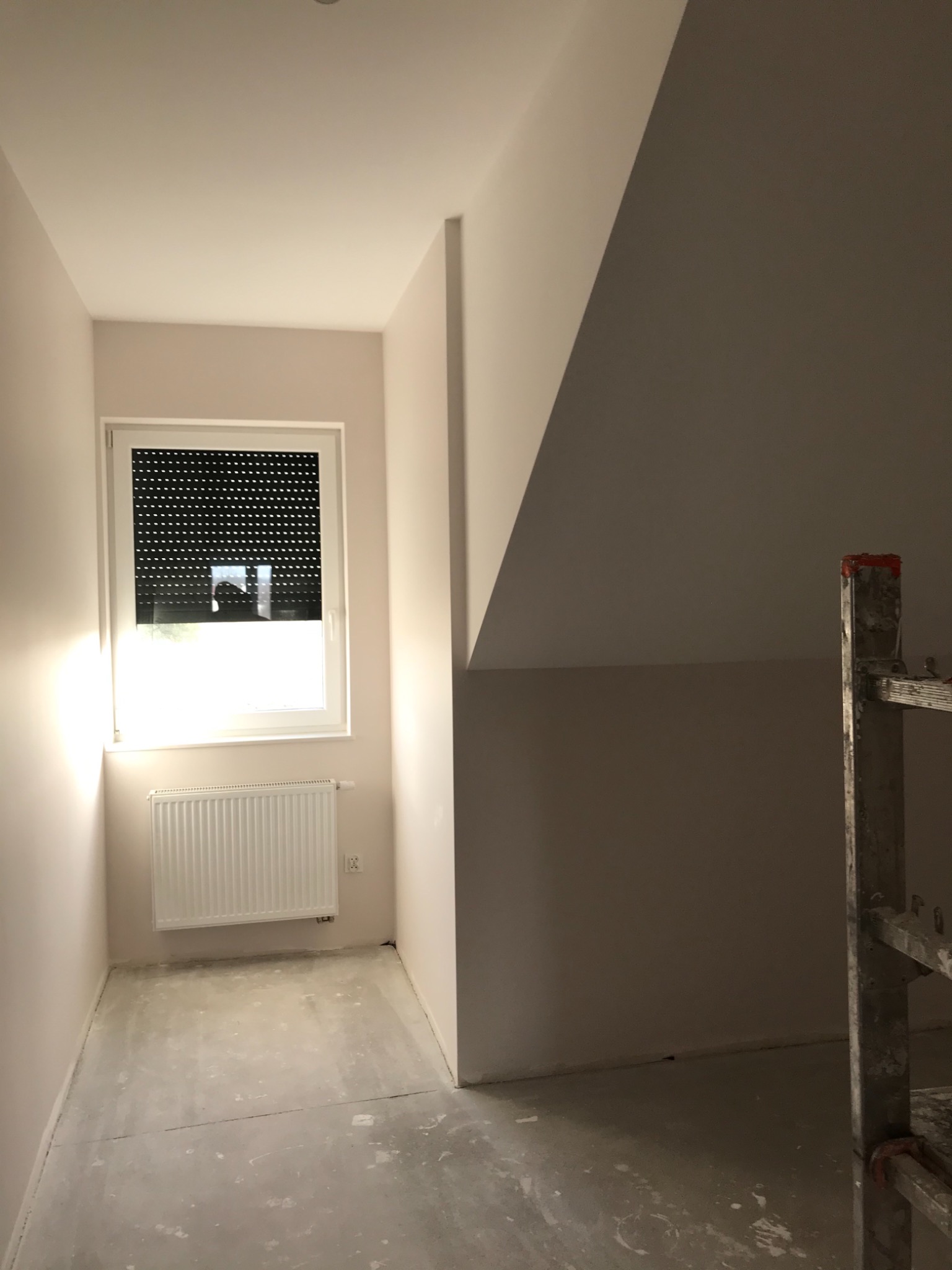 Pokój na poddaszu po świeżym pomalowaniu ścian na jasny, pastelowy kolor. Widoczne ślady po pracach na podłodze i drabina oparta o ścianę.