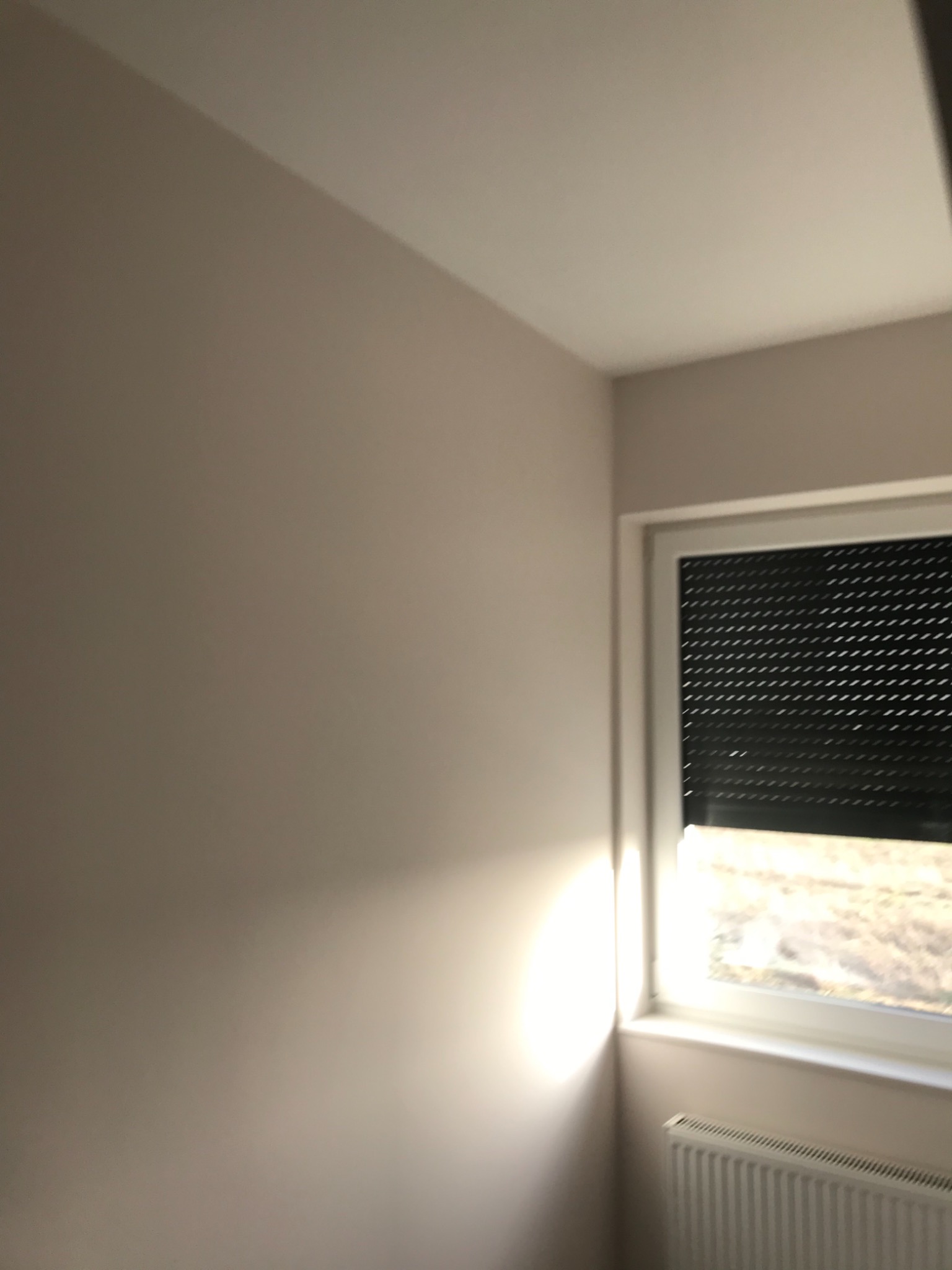 Świeżo pomalowane wnętrze pokoju w odcieniach beżu, z oknem z żaluzjami i grzejnikiem.