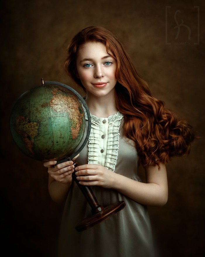 Portret młodej kobiety z rudymi włosami i niebieskimi oczami, trzymającej stary globus na ciemnym, teksturowanym tle.