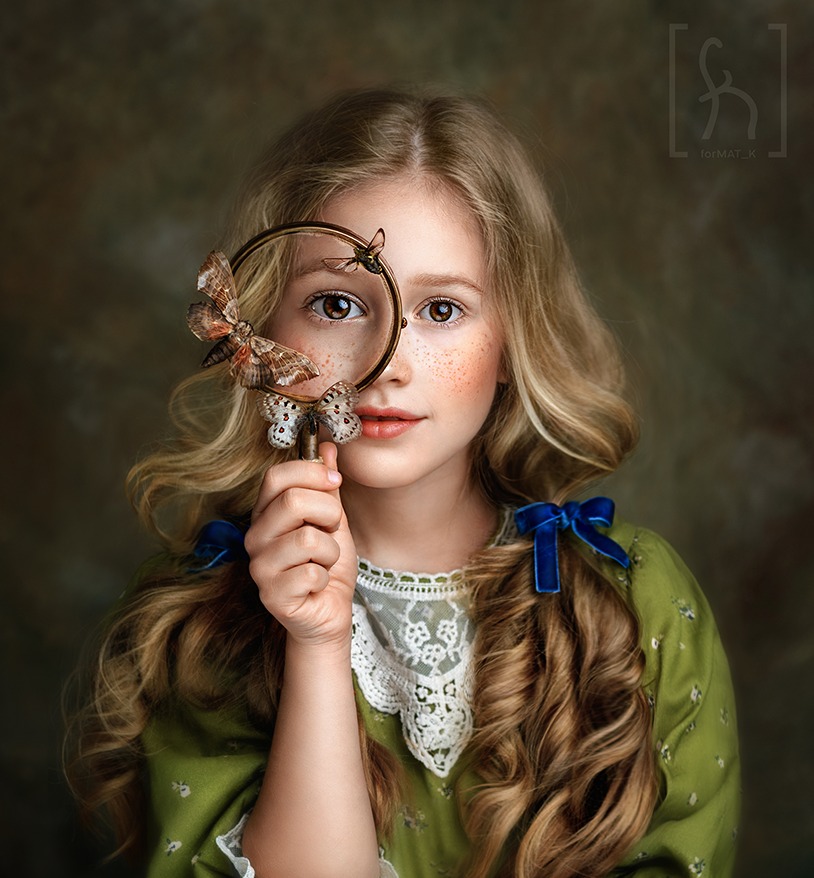 Portret dziewczynki z blond włosami i piegami, trzymającej lupę ozdobioną motylami, ubrana w zieloną sukienkę z koronkowym kołnierzem.