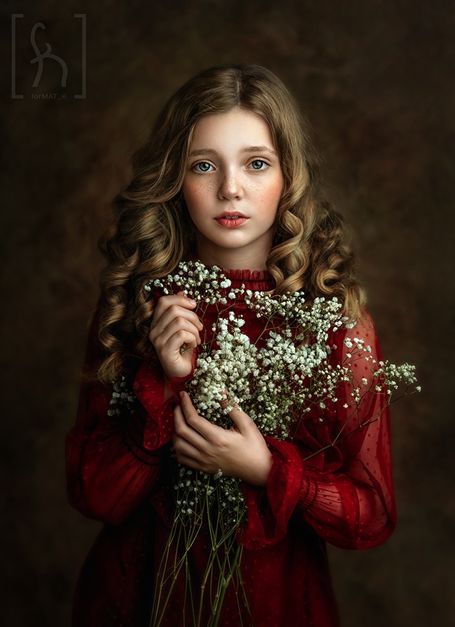 Portret dziewczynki z piegami, w czerwonej sukience, trzymającej bukiet gipsówki na ciemnym tle.