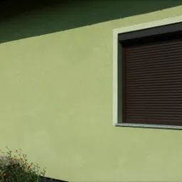 Brązowa osłona okienna i drzwiowa na elewacji w kolorze pistacjowym, widoczne w zamkniętej pozycji, z detalami faktury tynku i oświetlenia zewnętrznego.
