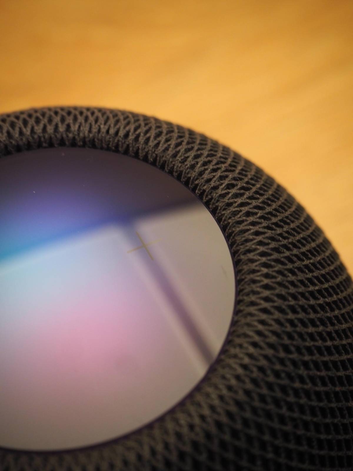 Zbliżenie na głośnik inteligentny HomePod Mini z widoczną siatką tekstylną i refleksami światła na powierzchni dotykowej, z drobnym zarysowaniem w kształcie krzyżyka.