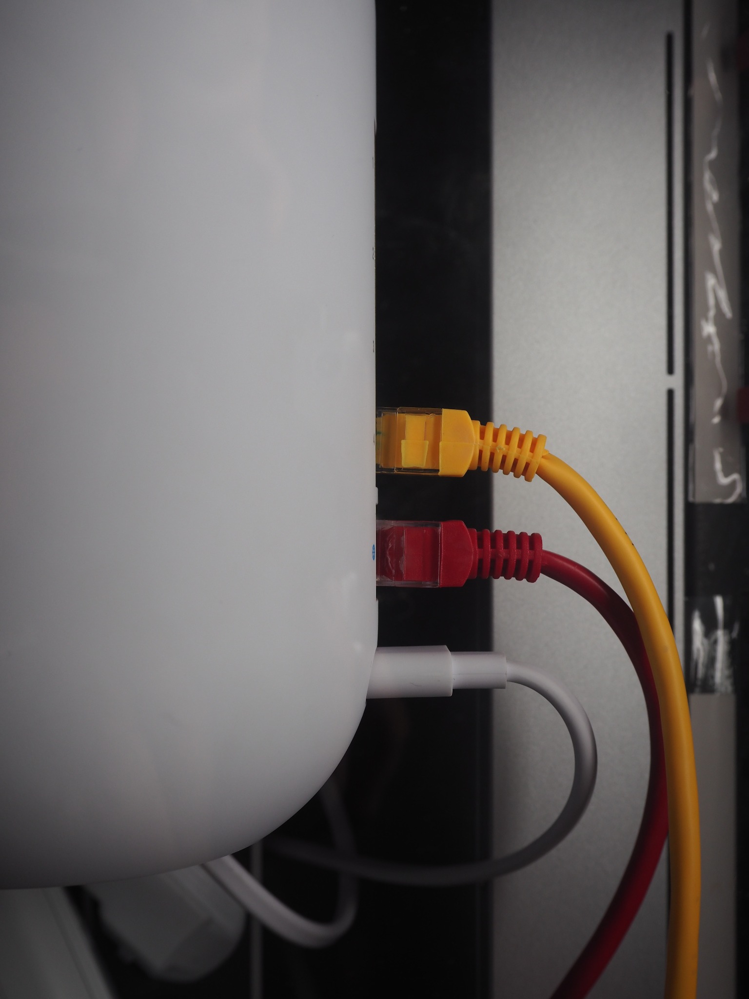 Dwa kable sieciowe RJ45 - żółty i czerwony - podłączone do białego urządzenia sieciowego, widoczne w ciemnym otoczeniu.