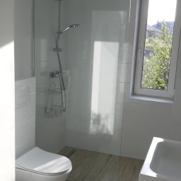 GRASTONE Emilian Stasiuk - Nowoczesna łazienka z kabiną prysznicową typu walk-in, podwieszaną toaletą i drewnopodobną podłogą z odpływem liniowym.