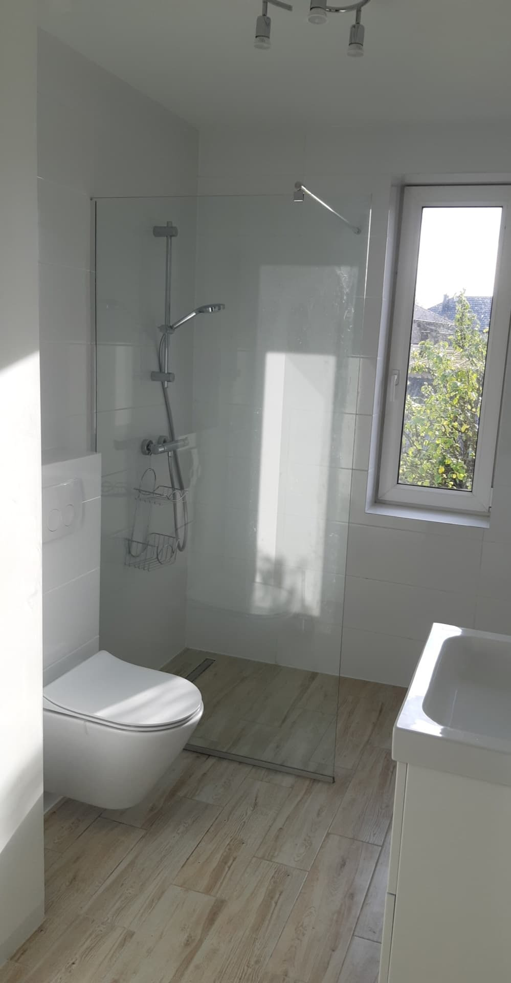 Nowoczesna łazienka z kabiną prysznicową typu walk-in, podwieszaną toaletą i drewnopodobną podłogą z odpływem liniowym.