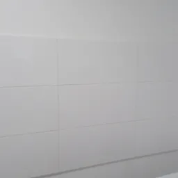 Białe, prostokątne płytki ceramiczne na ścianie nad wanną, widoczne fugi i krawędź wanny.