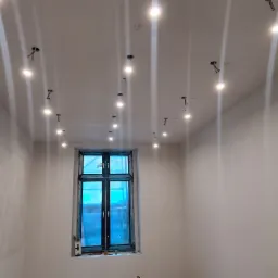 Wnętrze kamienicy z widocznymi punktami świetlnymi w suficie podwieszanym oraz oknem zabezpieczonym folią malarską.